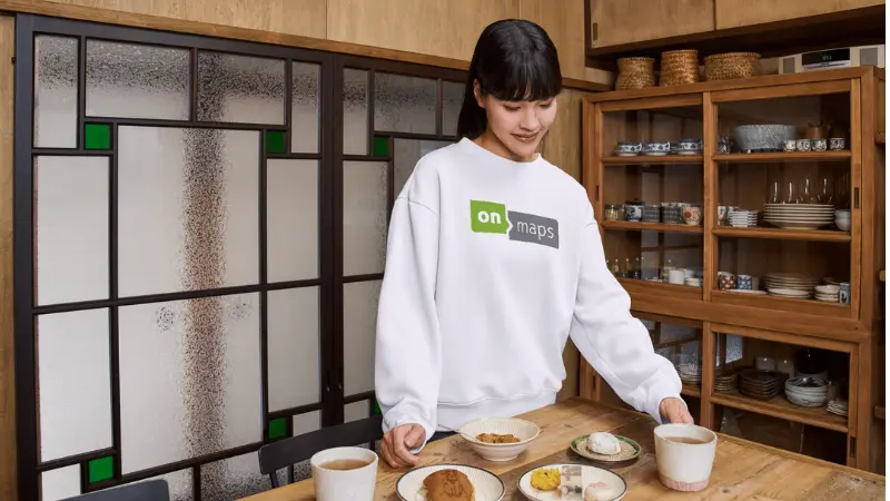 Person trägt Pullover mit onmaps-Logo beim Frühstück am Tisch