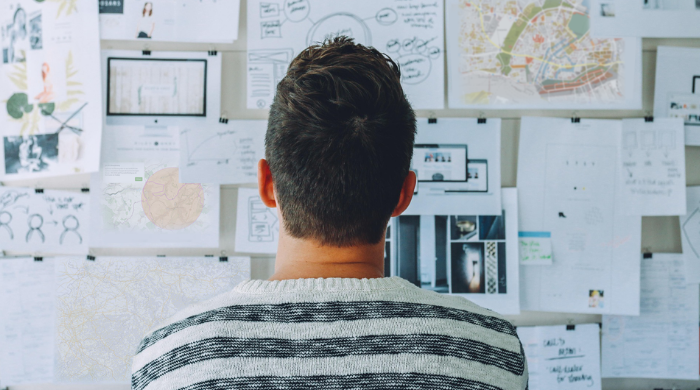 Kreative Konzeptphase: Analyse und Ideenfindung mit Karten, Diagrammen und Notizen auf einer Planungswand Person von hinten betrachtet eine Wand voller Pläne, Karten, Skizzen und Notizen – kreative Arbeitsumgebung oder Projektplanung