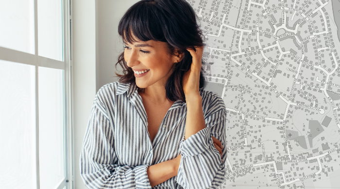 Architektur trifft Kartografie – Stadtplanung mit präzisen Geodaten Lächelnde Architektin oder Stadtplanerin steht vor einem Fenster, im Hintergrund ein detaillierter Stadtplan